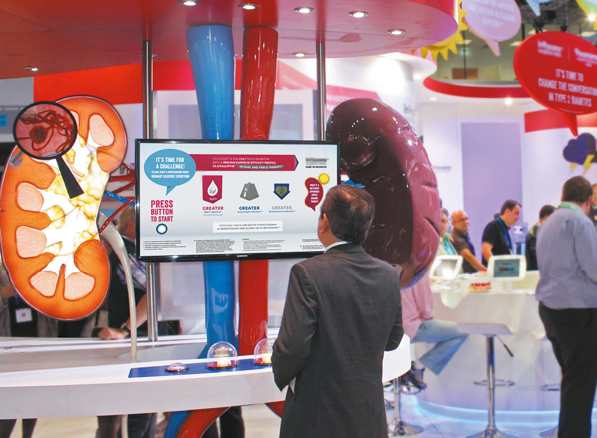 A large-scale exhibition booth for J&J shows a male delegate looking at a large interactive engagement activity. THe screen is triggered by pressing large bowls of sugar